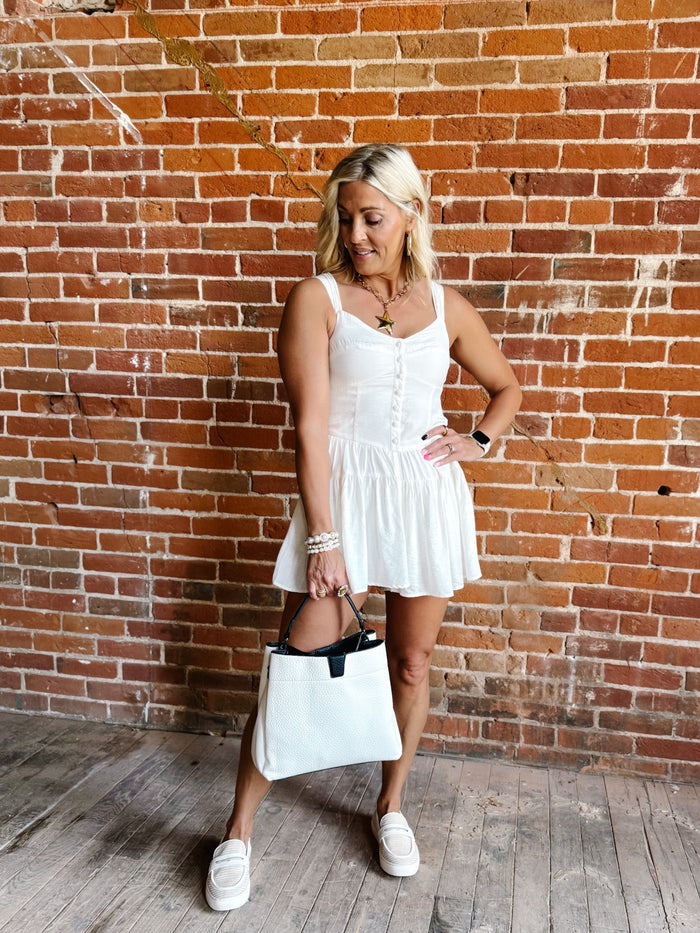 White romper with a sweetheart neckline and tiered skirt, worn by a woman standing against a brick wall.